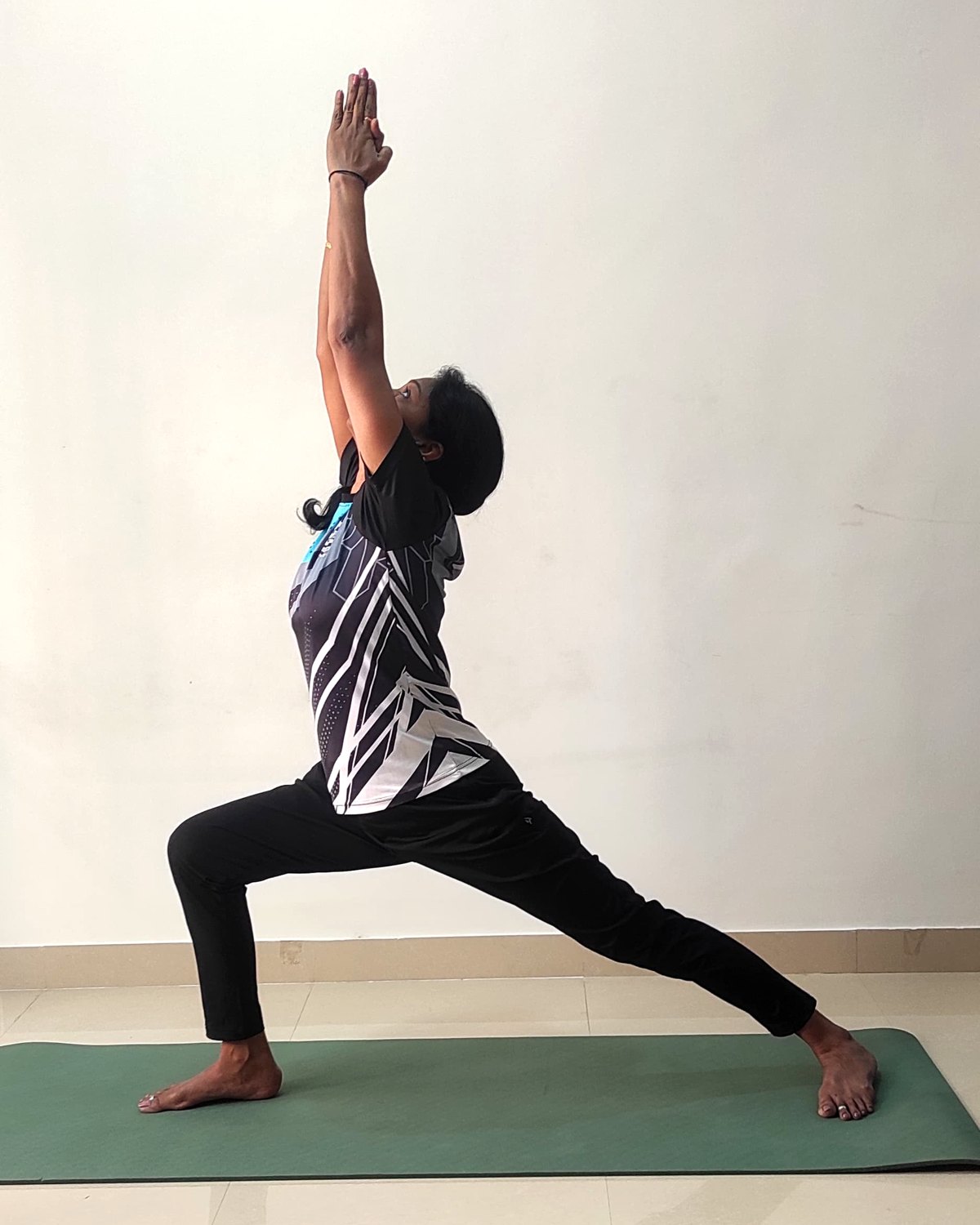 A standing warrior pose on a mat, both arms reaching overhead