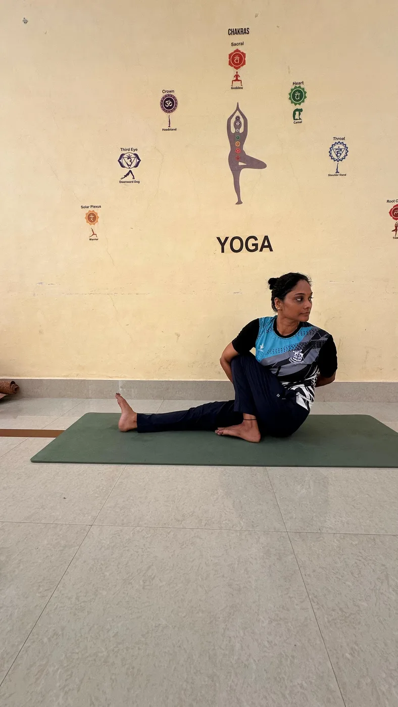 A seated spinal twist on a green mat, in a studio with a painted chakra wall