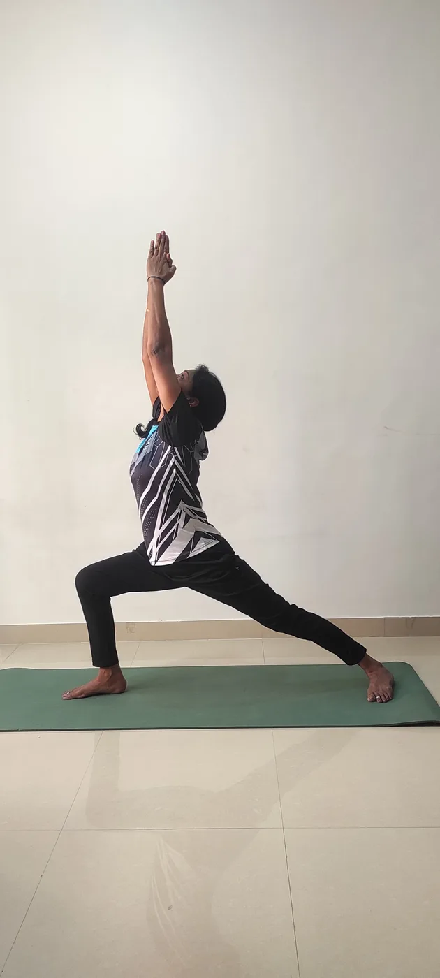 A standing lunge with both arms extended overhead on a yoga mat